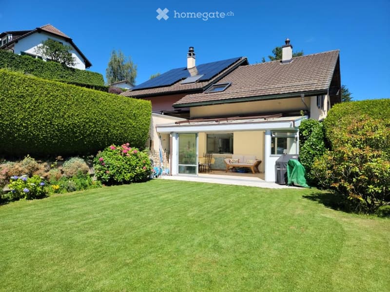 Two-story house with a well-maintained garden, solar panels on the roof, and a covered patio area with outdoor furniture.
