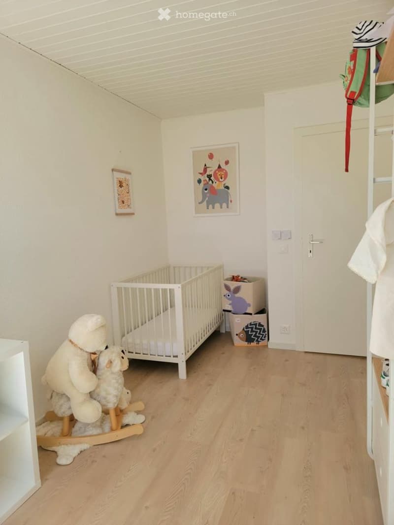 A well-lit, modern nursery with a white crib, rocking horse with stuffed animals, storage boxes, and decorative artwork on the walls.