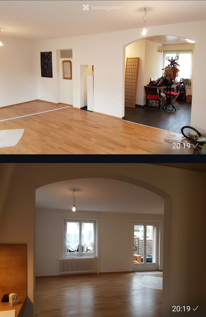 Empty living space with wooden flooring, white walls, and large windows. The room is completely unfurnished, showing only the basic structure and natural light.