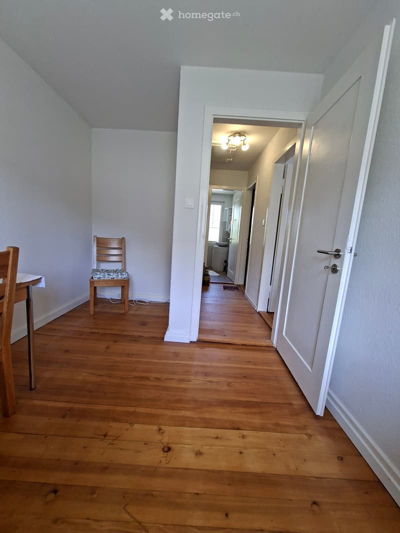 Empty hallway with wooden flooring, white walls, and a partially open door leading to another room.