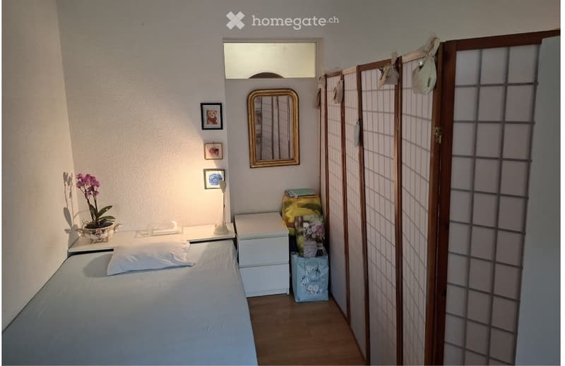 Cozy bedroom with a single bed, nightstand, mirror, flower vase, picture frames, and a screen divider.