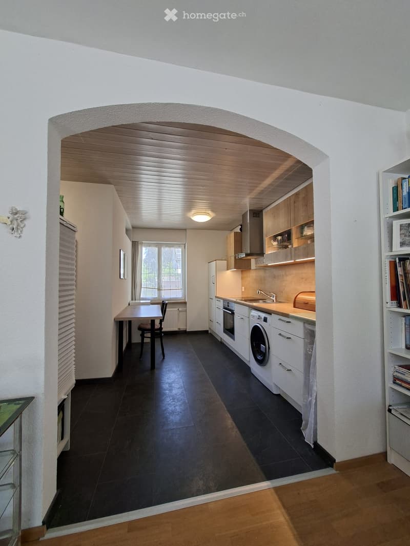 Modern kitchen with white cabinets, stainless steel appliances, dark tiled floor, and a small dining area with a table and chair.