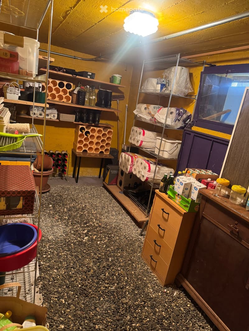 Storage room with shelves, wine rack, table, and various household items. The floor is covered with small pebbles.
