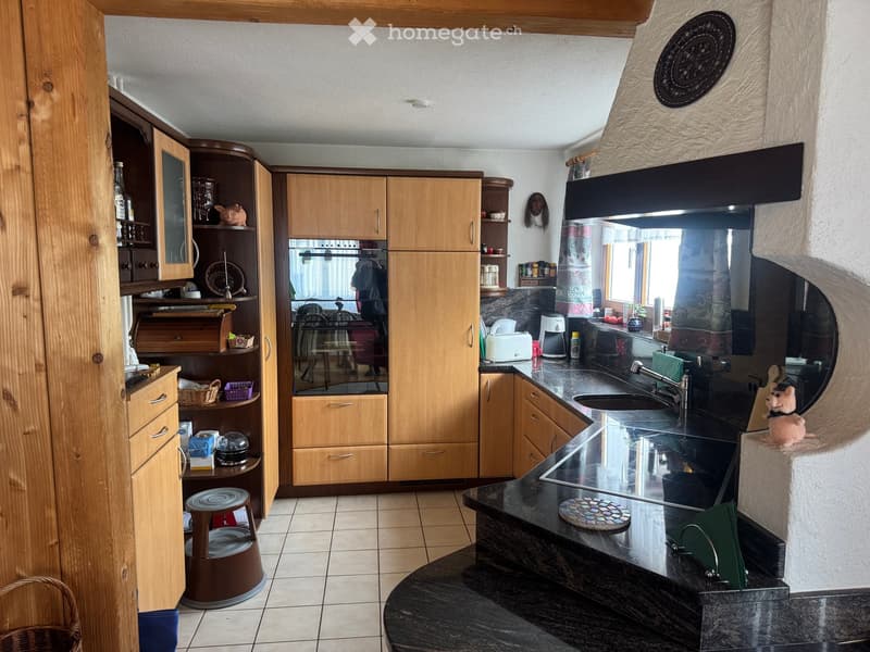 The kitchen features wooden cabinets, a black countertop, a sink with a faucet, a toaster, a coffee maker, and a small round stool. There is also a mirror on the wall and a small round table in the corner.