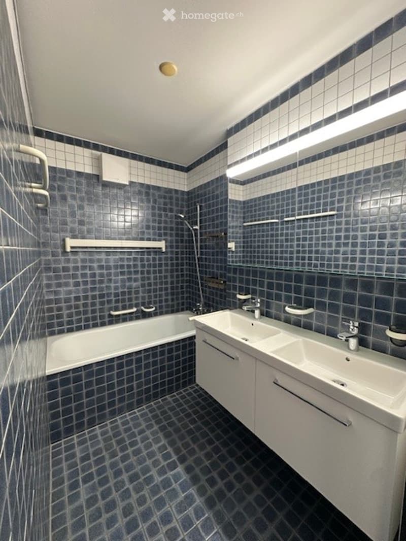 Bathroom with blue tiles, white bathtub, double sinks, and a mirror.