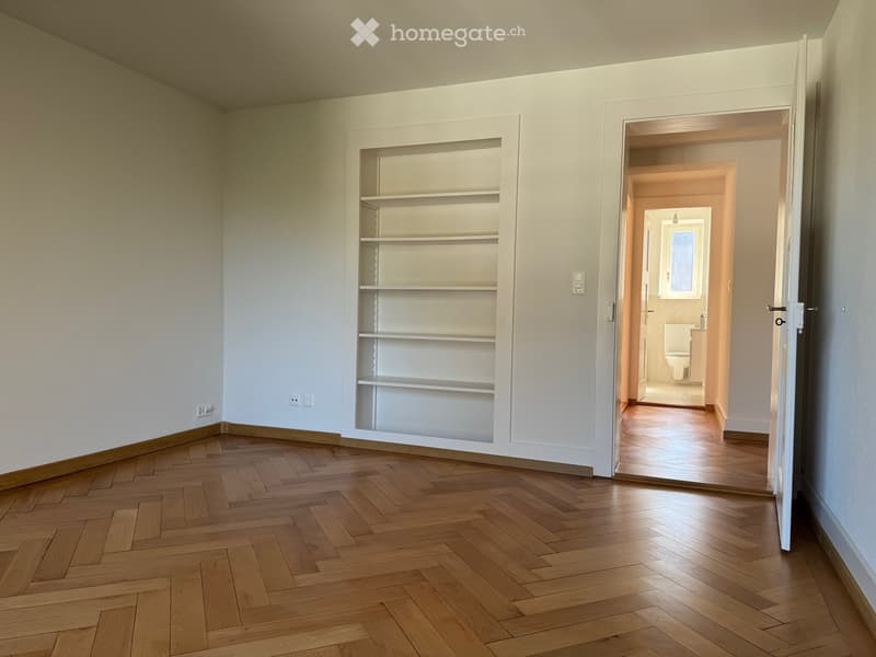 empty room, wooden parquet floor, white walls, built-in shelf, open door to bathroom