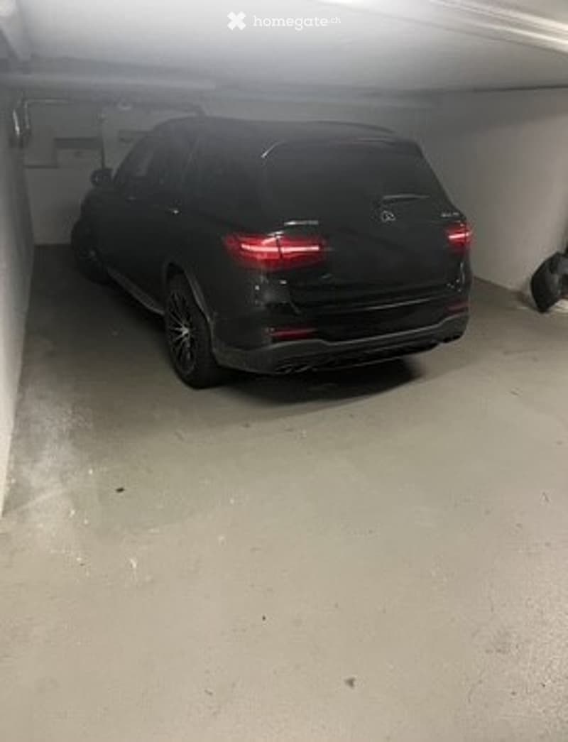 A black SUV is parked inside a garage with concrete floors and walls.