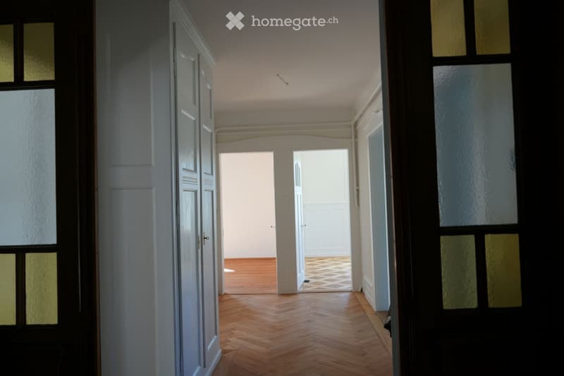 Empty hallway with wooden parquet flooring, white walls, and two doors leading to other rooms.
