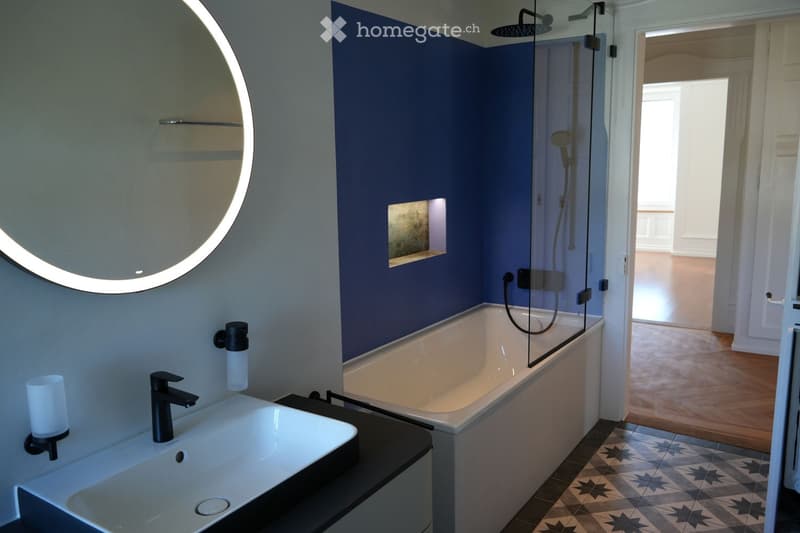 modern bathroom with blue wall, white bathtub, white sink, round mirror, black faucet, shower