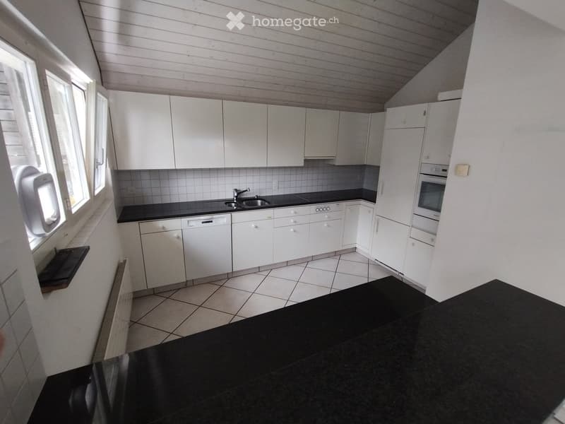 Modern kitchen with white cabinets, black countertops, tiled floor, and built-in appliances including an oven and dishwasher.