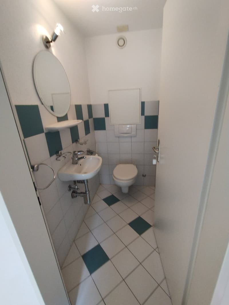 Small bathroom with white tiles, a sink, a toilet, a mirror, and a light fixture on the wall.