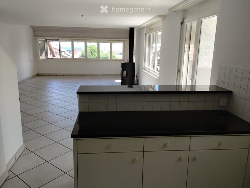 Empty kitchen with white tiled floor, white cabinets, black countertops, and a wood-burning stove in the background.