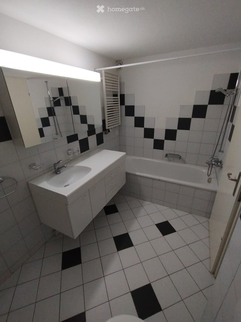 Bathroom with white tiles, black accents, a sink with a mirror, a bathtub, and a radiator.