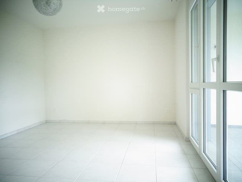 Empty room with white tiled floor and walls, large glass door leading outside, and a hanging spherical light fixture.