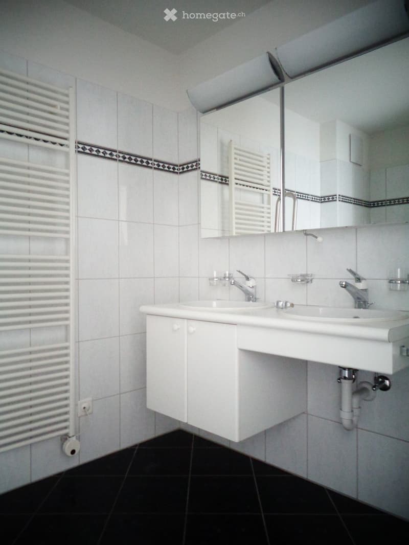 Modern bathroom with white tiles, black floor, double sink, mirror, and radiator.