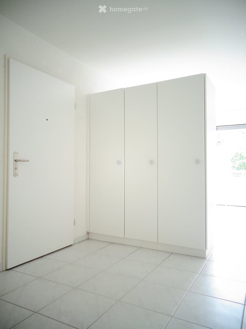Empty room with white tiled floor and white cabinetry along one wall, featuring a door and a window letting in natural light.