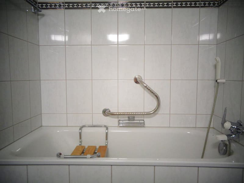 Bathtub with handrails and wooden seats, tiled walls, and a showerhead.