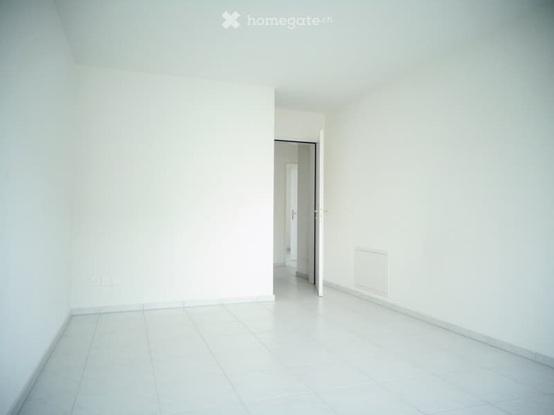 Empty room with white tiled floor and walls, featuring a doorway leading to another room.
