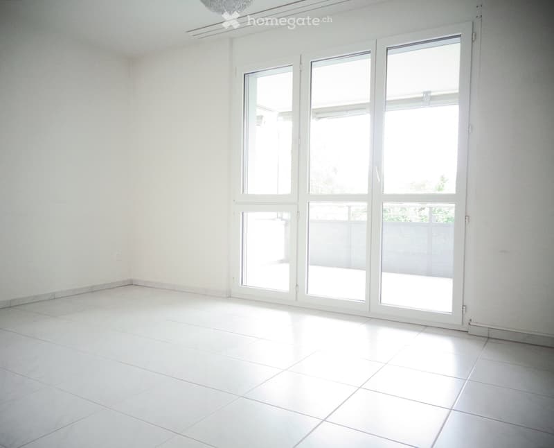 Empty room with white tiled flooring and large sliding glass doors leading to an outdoor area.