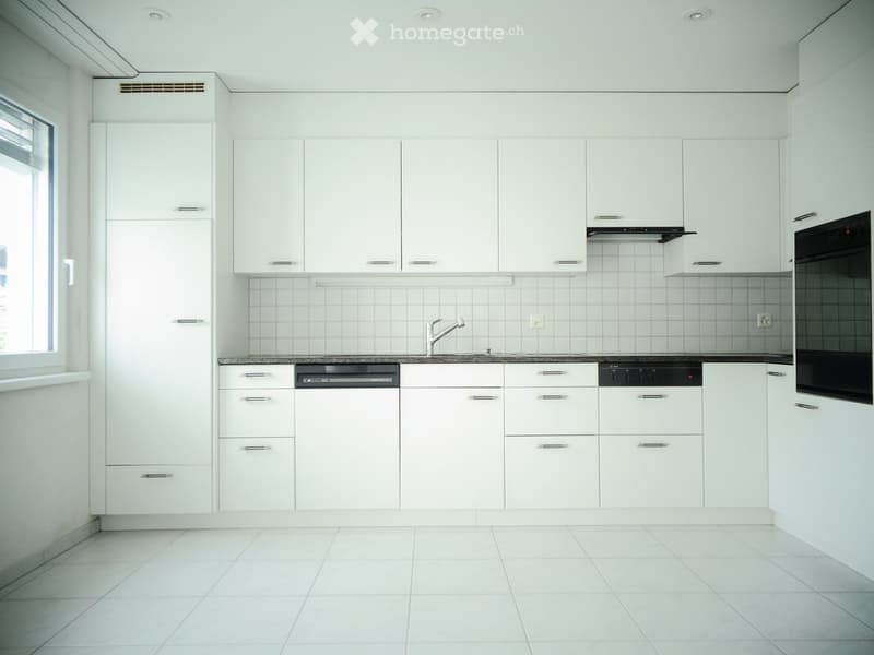 Modern kitchen with white cabinets, tiled walls, and stainless steel appliances including a dishwasher and oven.