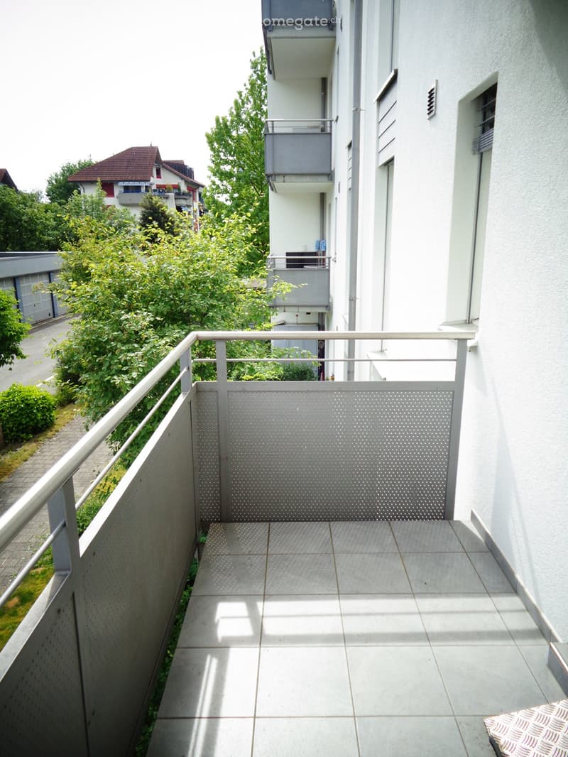 Balcony with tiled floor, metal railing, and view of neighboring buildings and greenery.