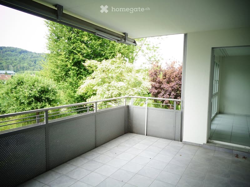 Balcony with tiled floor, metal railing, and a view of green trees and hills.