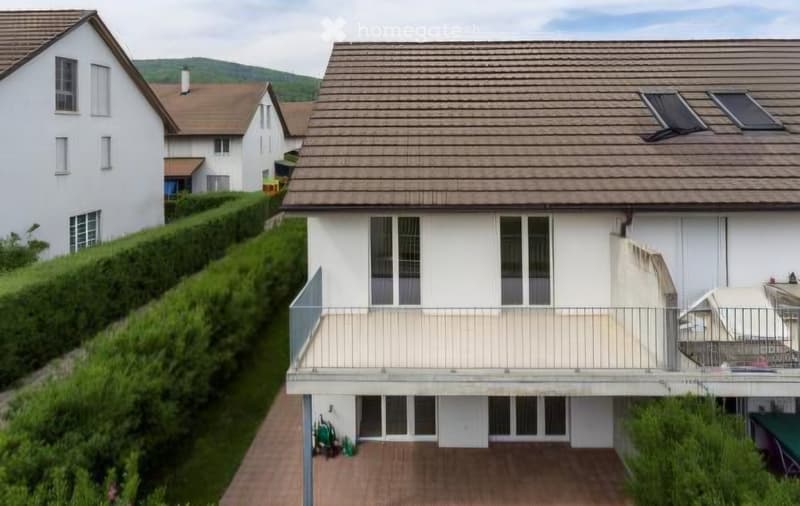 Two-story house with a modern design, featuring a balcony on the upper level, large windows, and a sloped roof with solar panels.