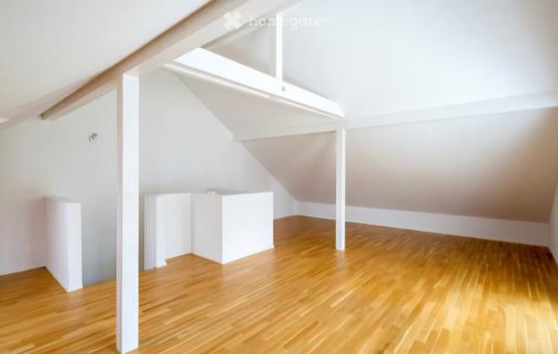 Empty attic space with wooden flooring, white walls, and exposed wooden beams. No furniture or equipment present.