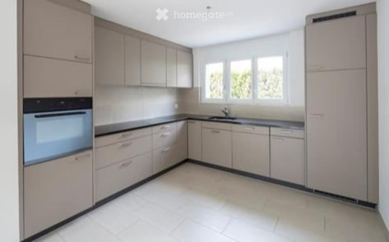 Modern kitchen with light-colored cabinets, a built-in oven, and a sink. The space is clean and well-lit with large windows.