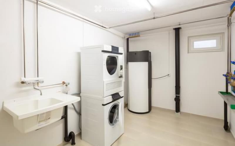 A small, modern bathroom with a white sink, faucet, washing machine, and refrigerator. The space is clean and well-lit with white walls and a light-colored floor.