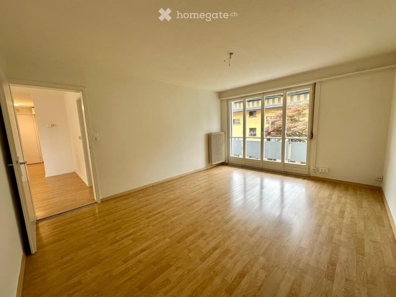 Empty room with wooden flooring, large sliding glass doors leading to a balcony, and a radiator on the wall.