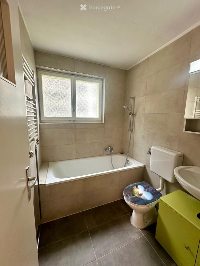 Bathroom with a bathtub, toilet, sink, and showerhead. Features a frosted window, radiator, and a green cabinet.