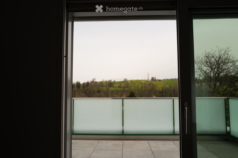 Balcony with modern glass railing, tiled floor, and scenic view of green hills and trees.