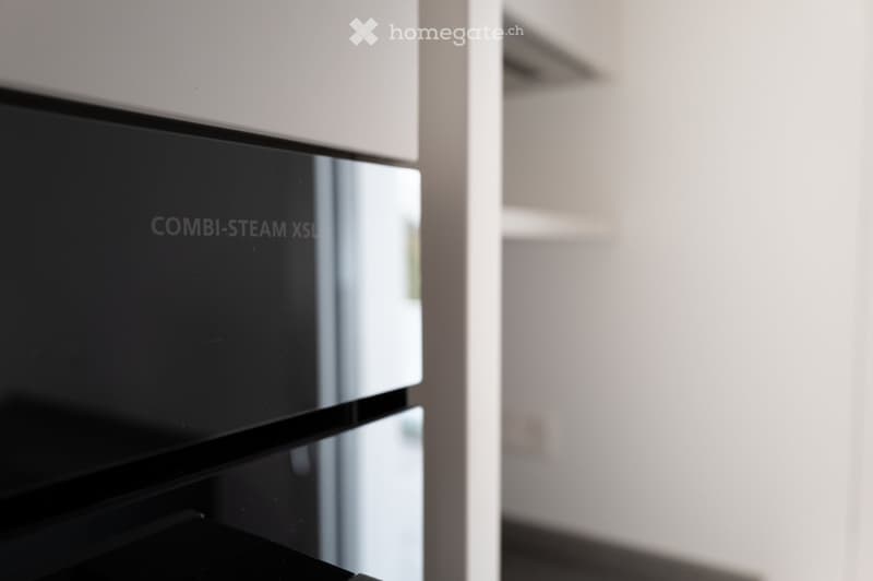 Modern kitchen with a sleek black oven featuring a reflective surface and a visible steam function label.