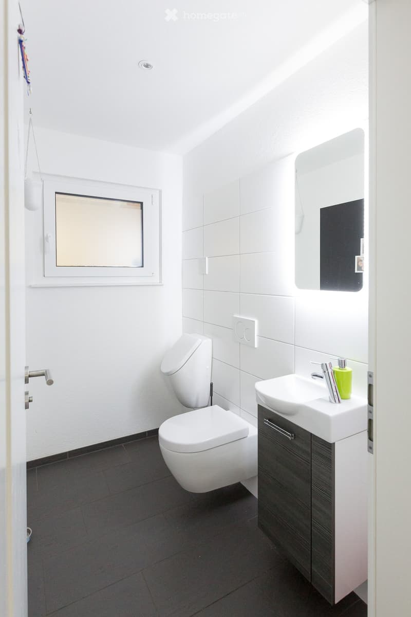Modern bathroom with white tiles, dark floor, toilet, sink with faucet, mirror, and cabinet.