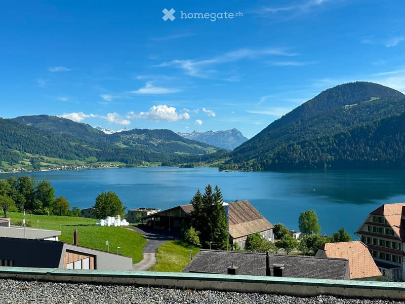Scenic view of a lake surrounded by mountains, with several houses and trees in the foreground.