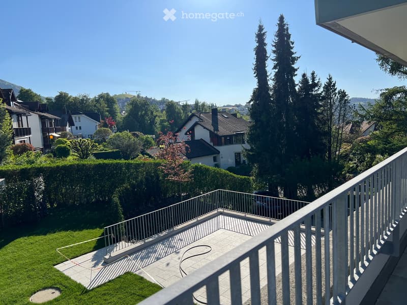Balcony overlooking a well-maintained garden with a lawn, hedges, and surrounding houses.