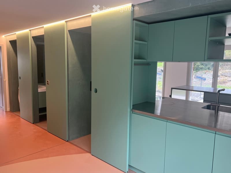 Modern kitchen with mint green cabinets, stainless steel countertop, and built-in sink.