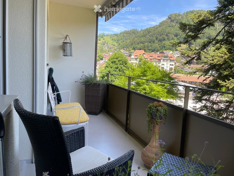 Balcony with wicker chairs, small table, potted plants, and scenic mountain view.