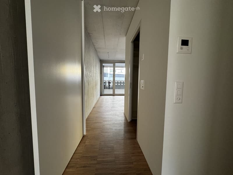 Empty hallway with wooden flooring, white walls, and a door leading to an outdoor area.
