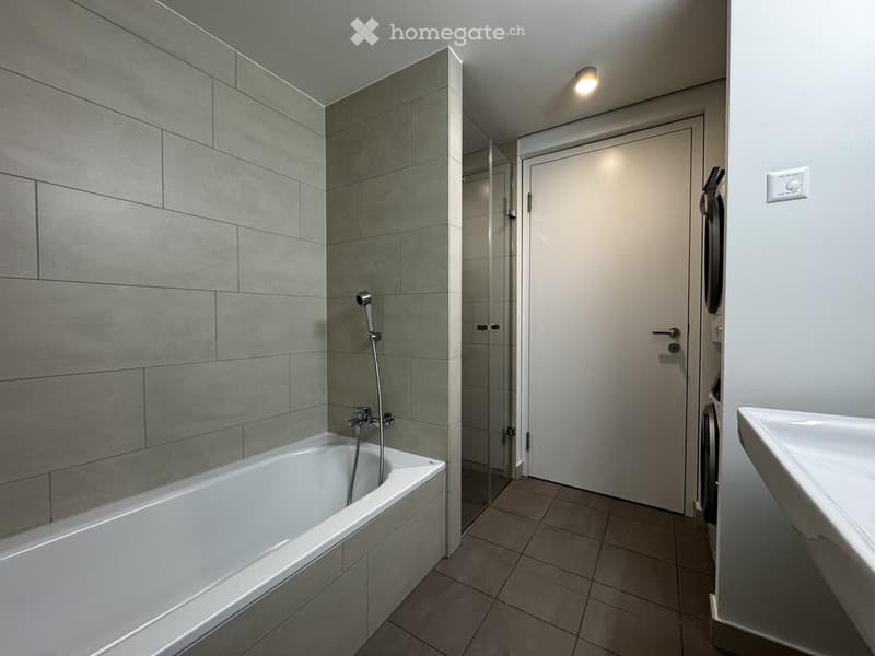 Modern bathroom with a bathtub, tiled walls, a glass-enclosed shower, and a sink.