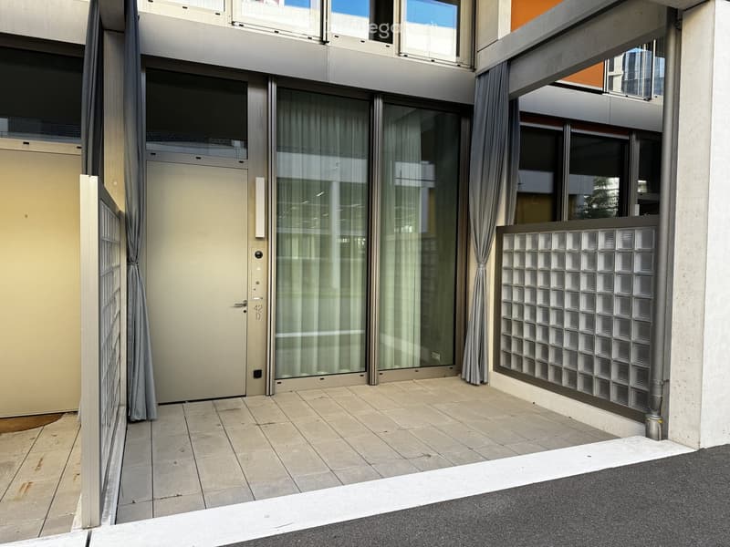 Balcony with tiled floor, glass sliding doors, curtains, and a decorative glass block wall.