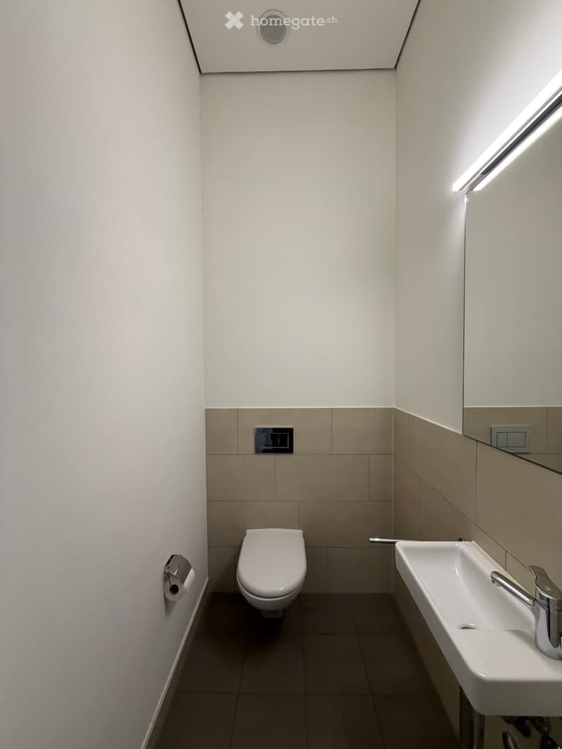 Modern bathroom with white walls, beige tiles, a toilet, a sink with a chrome faucet, and a mirror above the sink.