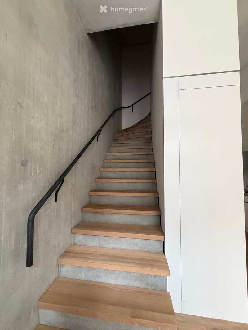 Modern staircase with wooden steps and concrete risers, featuring a black metal handrail.