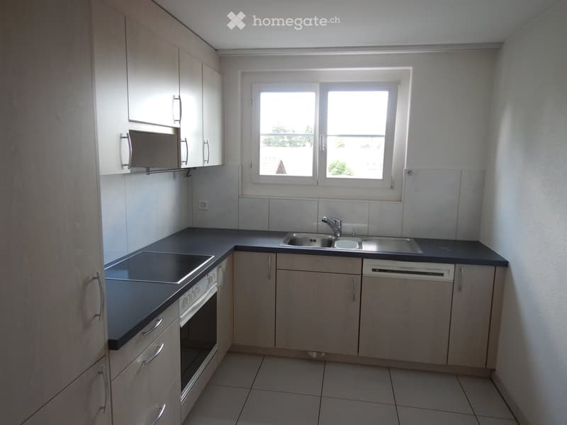 Modern kitchen with light wood cabinets, stainless steel sink, oven, and dishwasher. Features a large window with a view of greenery.