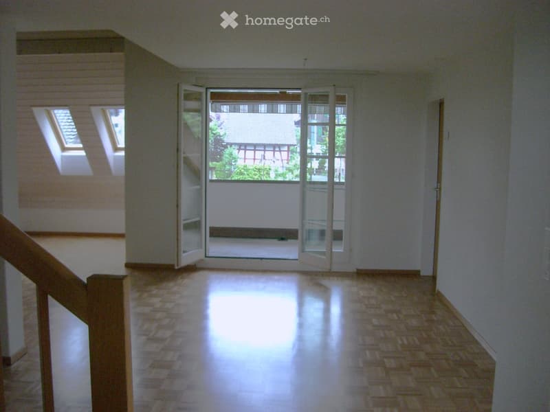 Empty room with wooden flooring, white walls, large glass doors leading to a balcony, and skylights in the ceiling.