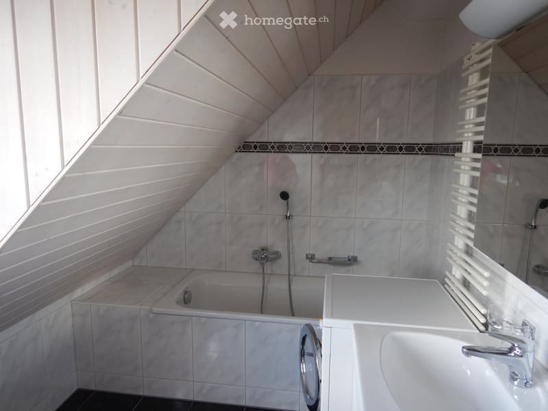 Modern bathroom with marble tiles, a bathtub, a sink, a mirror, and a radiator. The ceiling has a skylight and wooden beams.