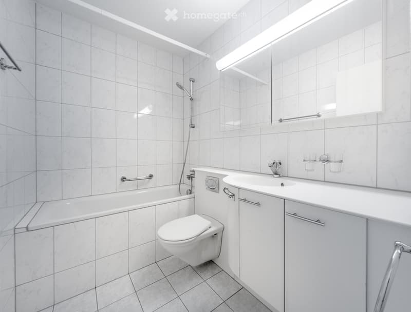 Tiled bathroom with a toilet, vanity sink, and shower area with a showerhead.