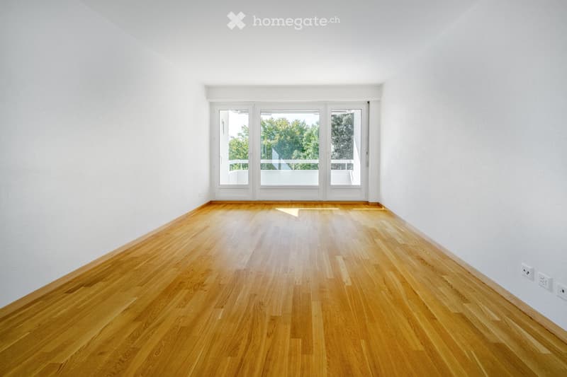 Empty room with light wooden flooring and white walls, featuring large glass doors leading to a balcony.