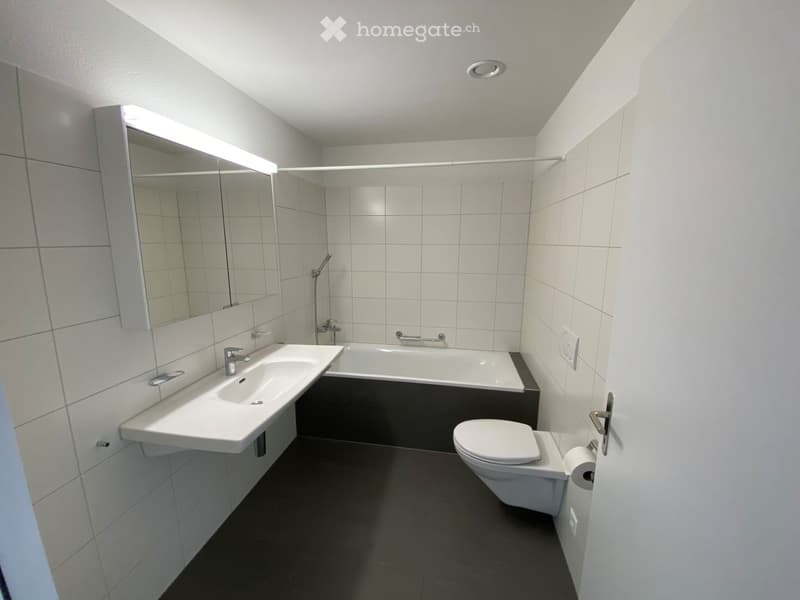 Modern bathroom with white tiles, a sink, bathtub, toilet, and a large mirror with built-in lighting.